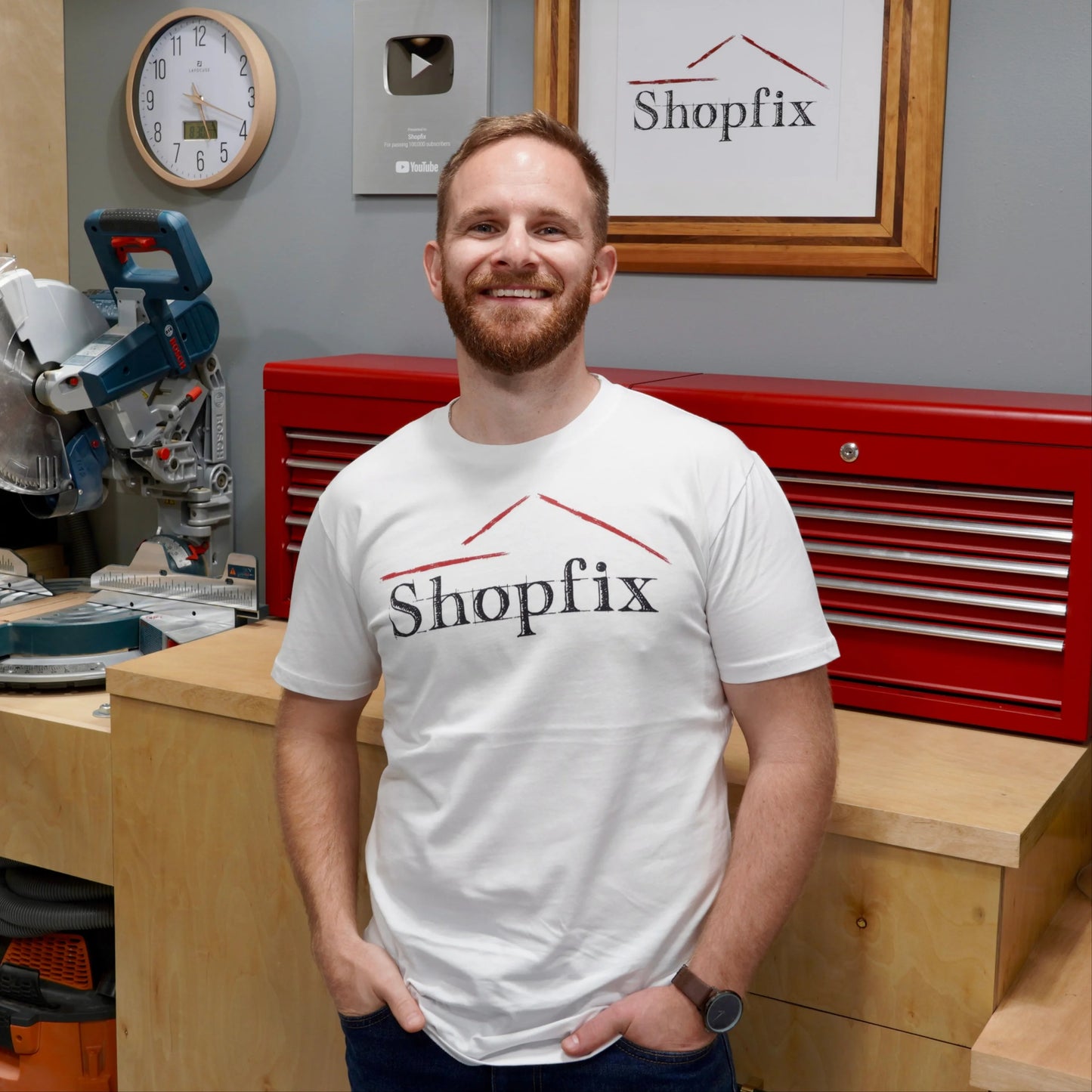 Man wearing a Shopfix t-shirt standing in a workshop with tools and equipment.