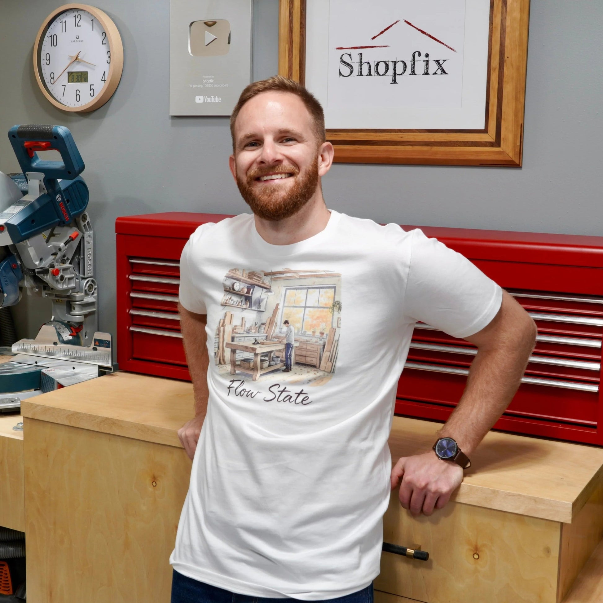 Man standing in a workshop with tools and 'Shopfix' branding on the wall.