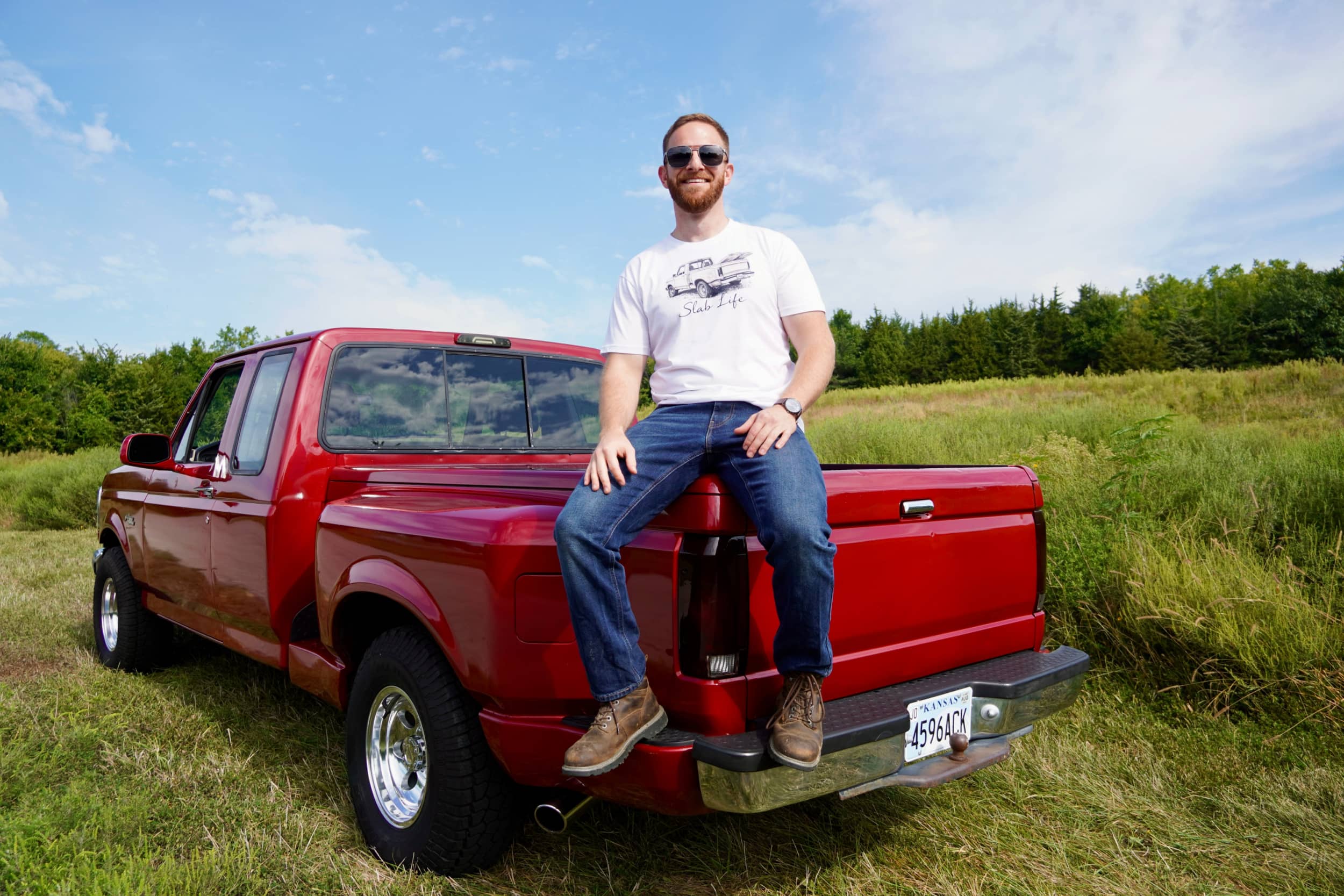 Red pickup truck with a man sitting on its tailgate.