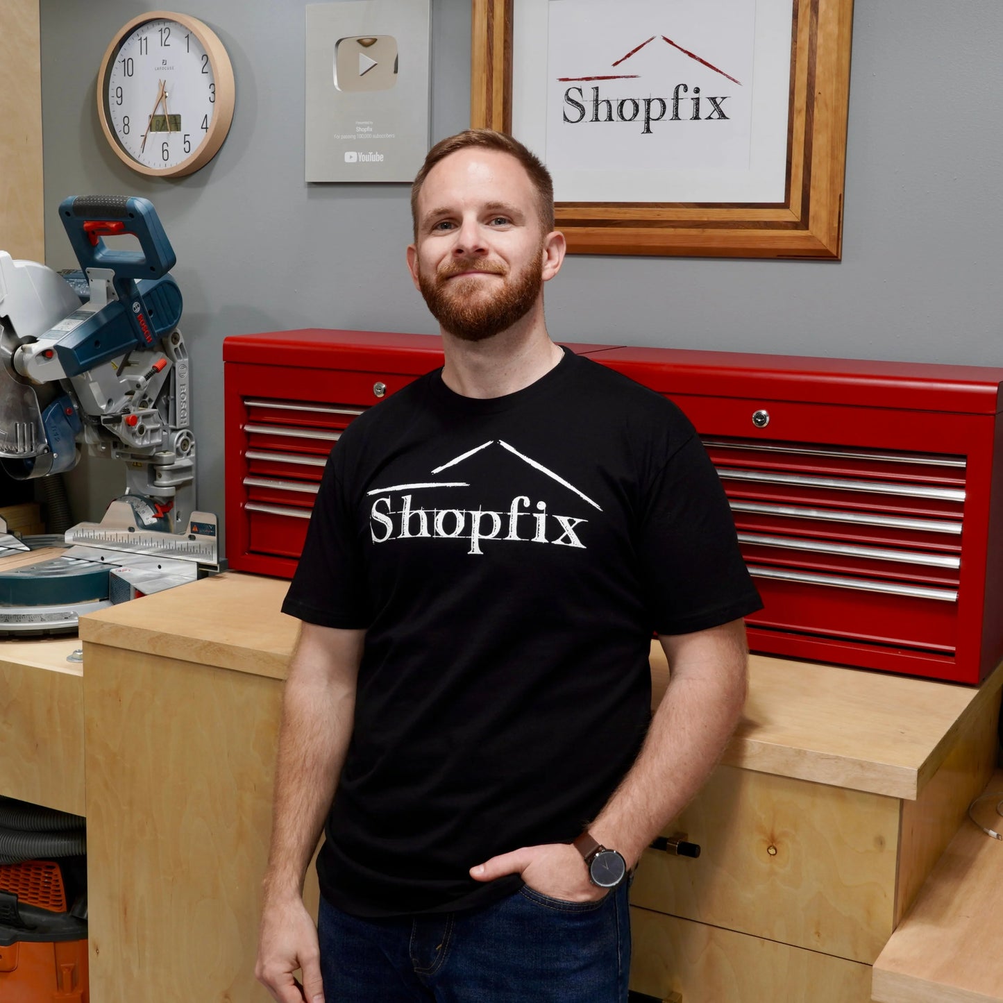 Man wearing a Shopfix shirt standing in a workshop with tools and equipment.