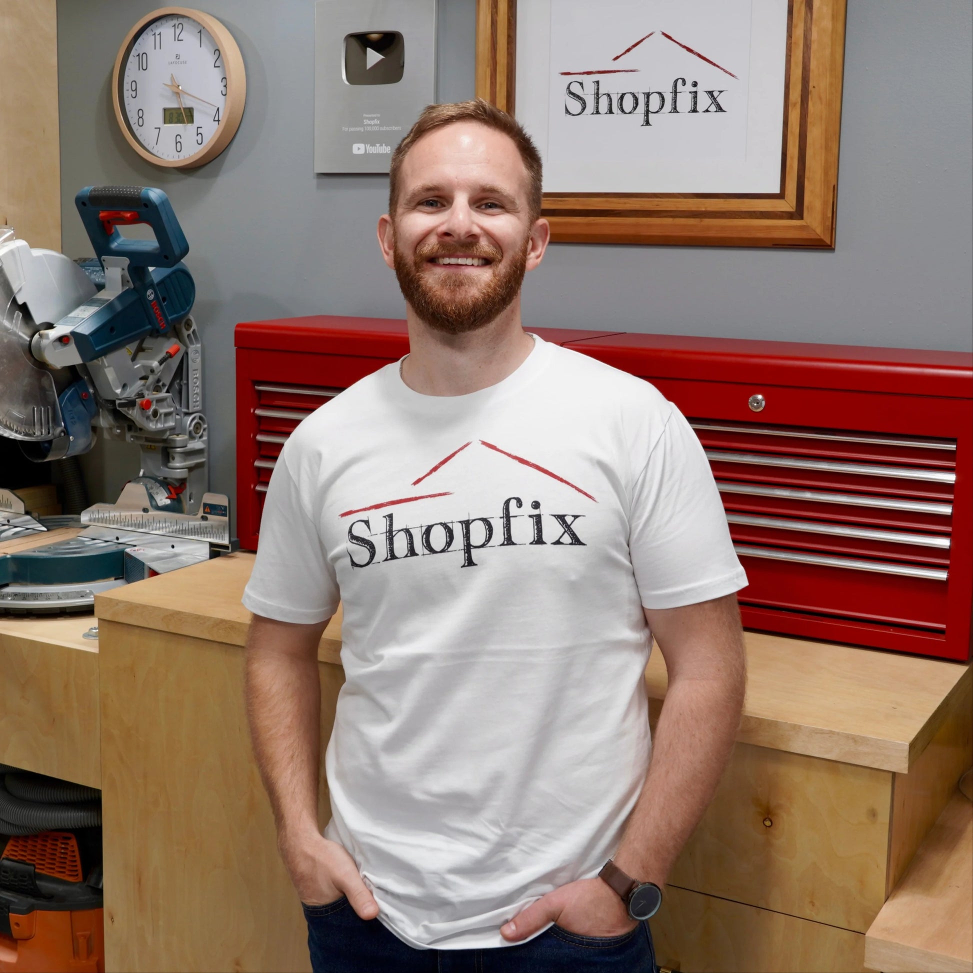 Man wearing a Shopfix t-shirt standing in a workshop with tools and equipment.